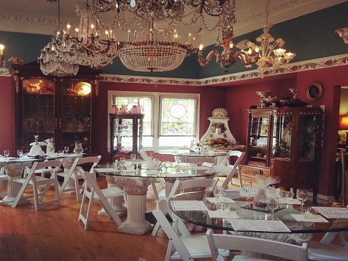 A dining room with white chairs and chandeliers where you can book a car for a wine tour.