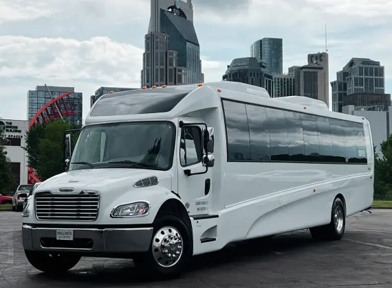 A white limo bus parked in front of a city.