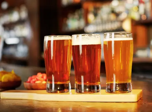 Three glasses of beer are lined up on a wooden bar at a transportation service.