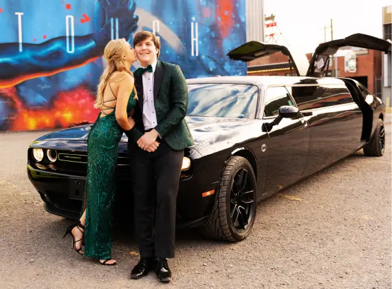 A man and woman standing next to a challenger black limo, representing a luxury transportation service.