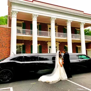 A newly-wed couple are standing beside a black dodge challenger stretch limo of Nashville Chauffeur INC.