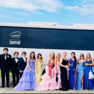 A group of teens is standing beside the white party bus of Nashville Chauffeur INC.