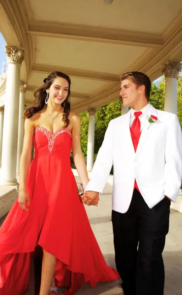 A girl in red and a boy in a white formal outfit are enjoying prom limo rental