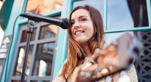 A young woman playing an acoustic guitar in front of a microphone.