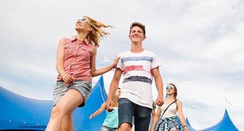 A group of people walking through a grassy field at a music festival.