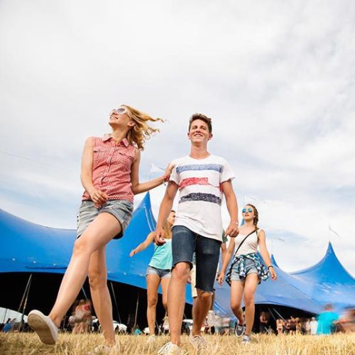 A group of people walking through a grassy field at a music festival.