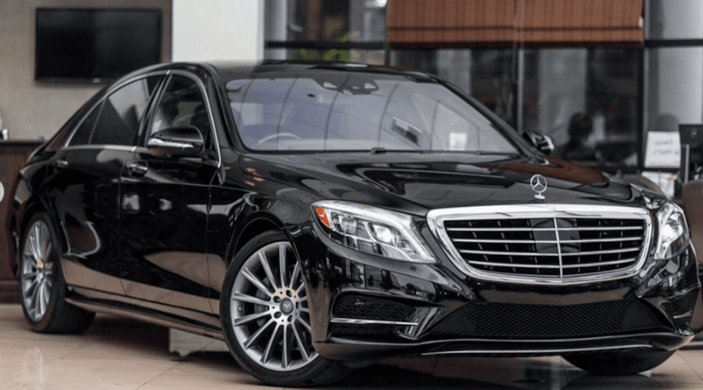 The black mercedes luxury car is parked in front of a building.